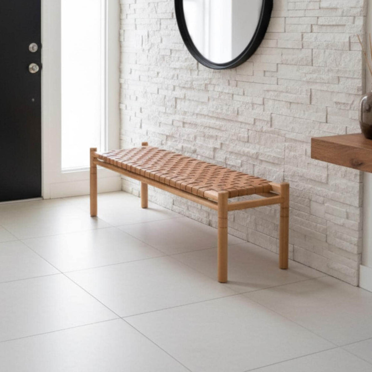 Wooden bench with woven seat against a white brick wall.
