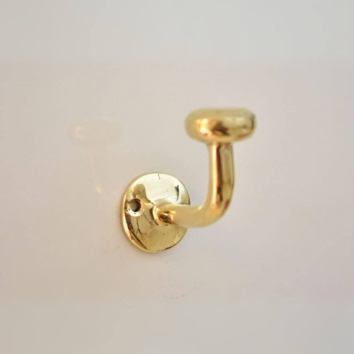 Gold brass wall hook on a light gray background