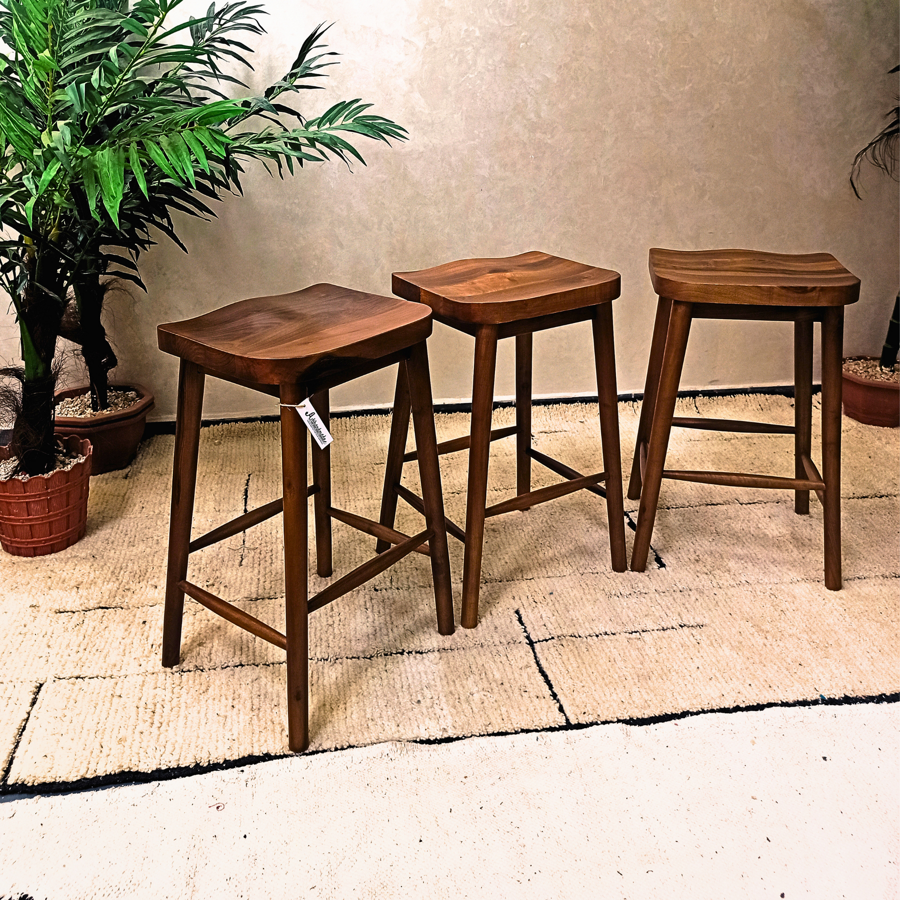 Three wooden bar stools on a textured floor with plants in the background